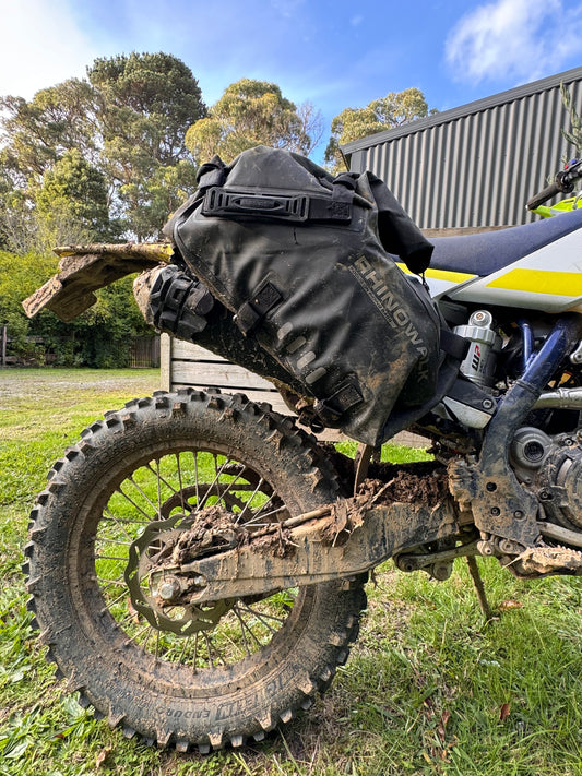 Rhino Walk Pannier Bags full of camping gear and properly fitted to an adventure motorcycle. The bike and bags are showing signs of use after a day adventure riding through challenging and muddy terrain. 